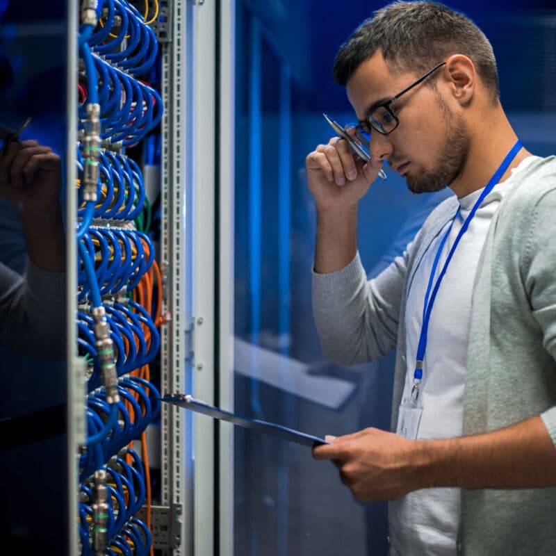 Data center technician reviewing a checklist while inspecting server rack cables